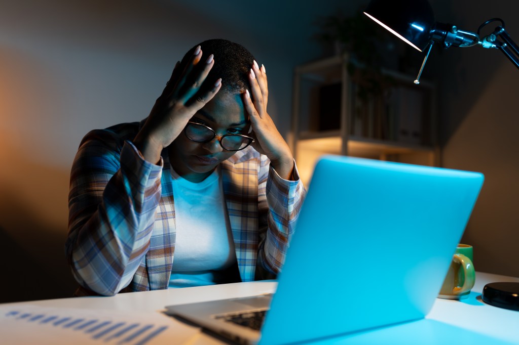 Black woman at laptop looking annoyed and has a headache.