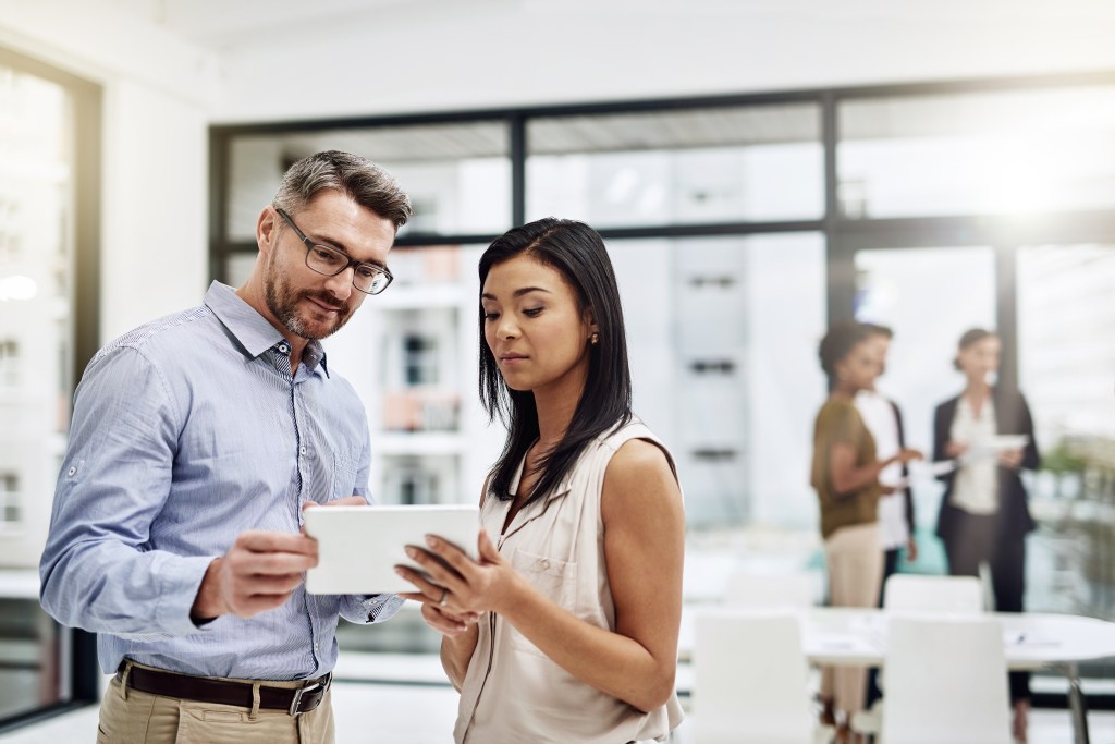 White man and Latin woman looking at a tablet at work.