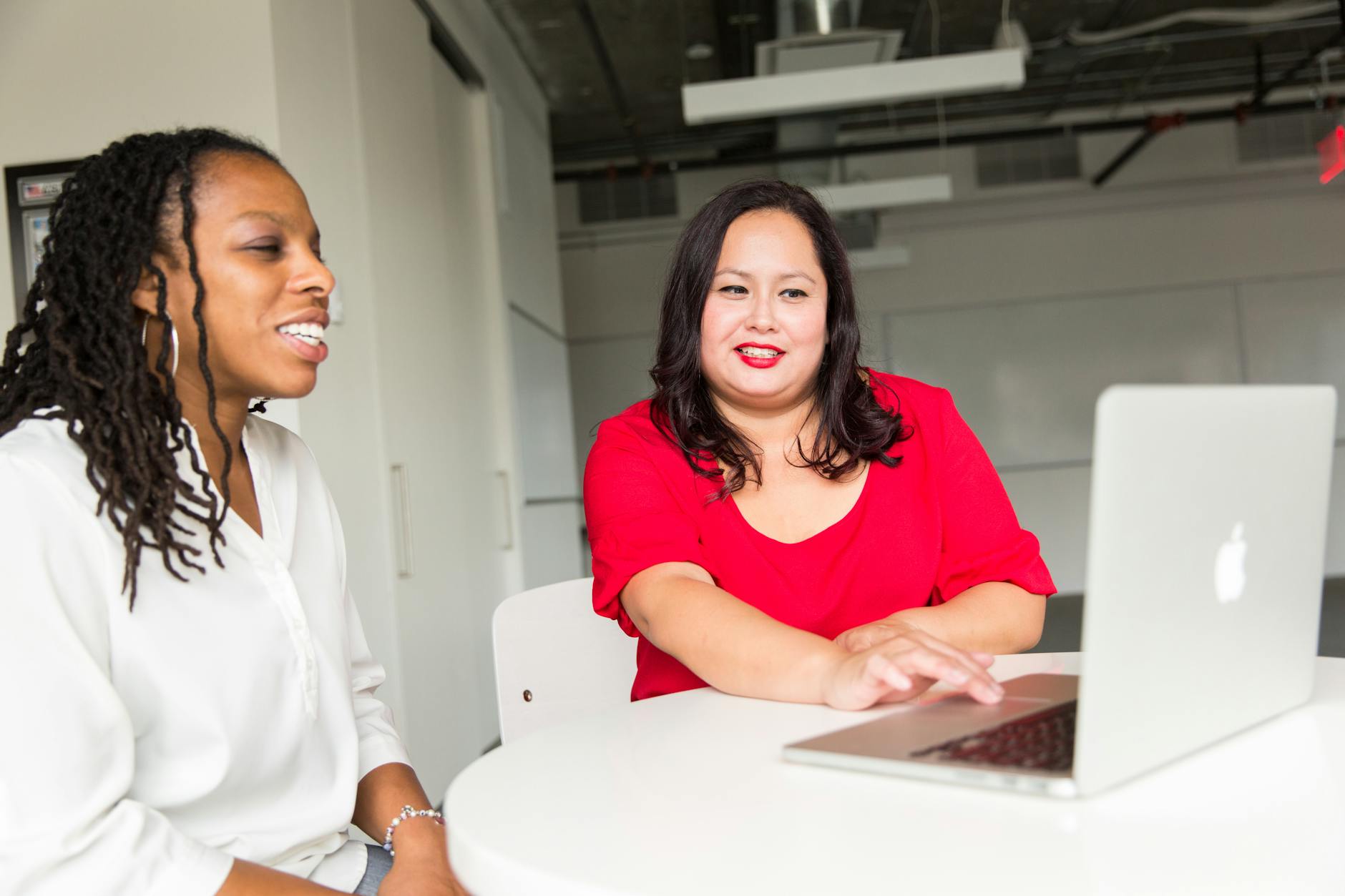 Black woman and Latina woman sitting at a table looking at a laptop.