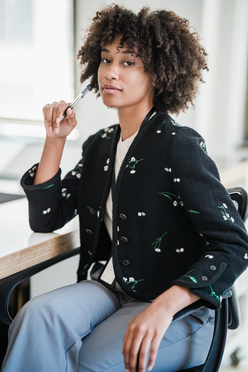 Mixed woman sitting down at a table wearing a floral jack and a name tag hanging from her neck.