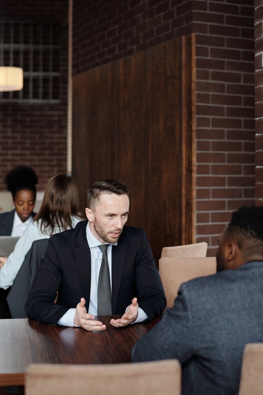 Black man and white man in suits sitting at a table talking.