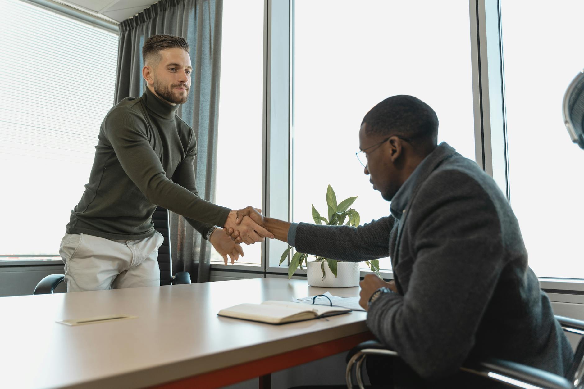 Black man sitting at desk shaking hands with white employee.