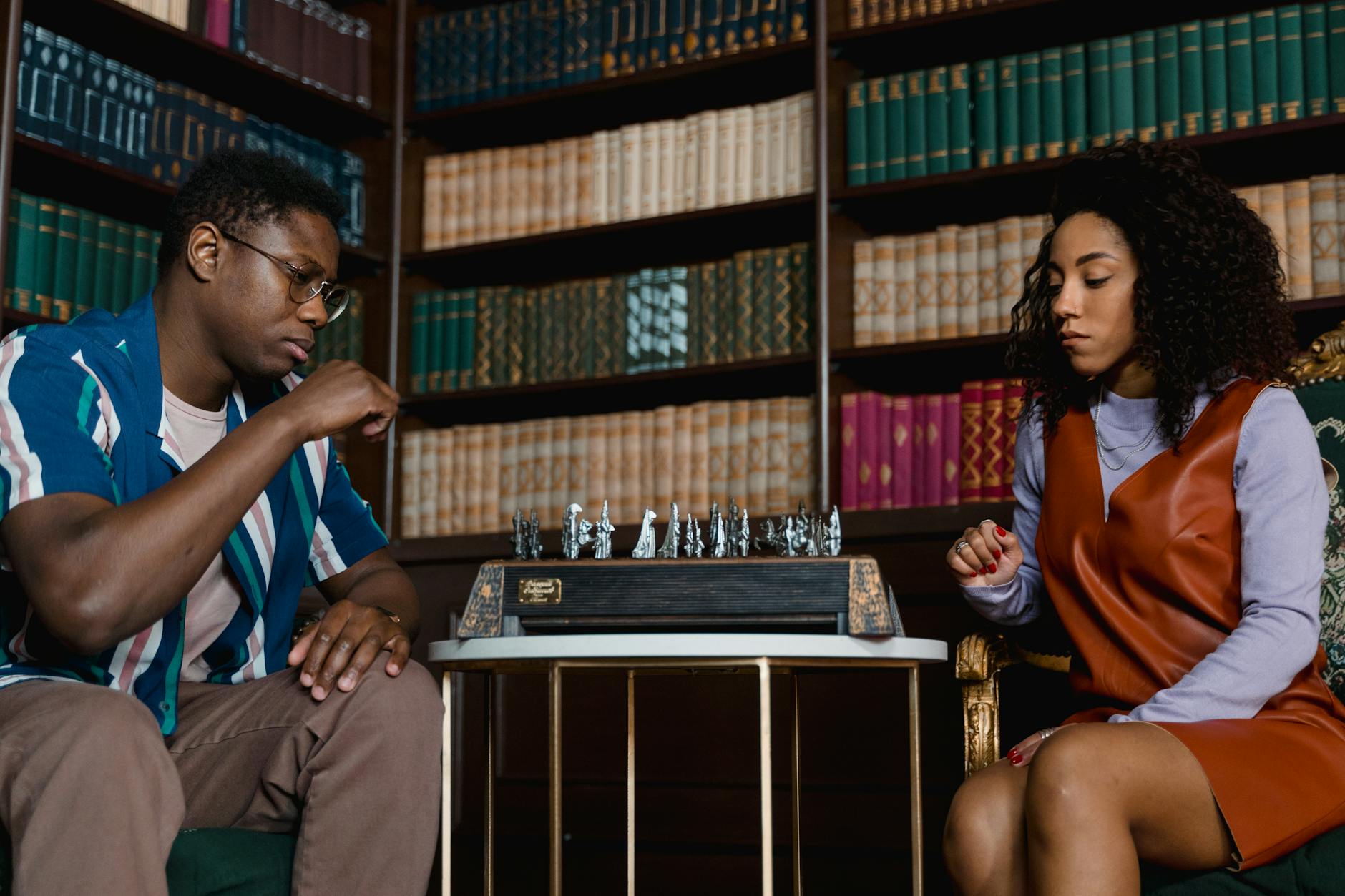 Black man and woman sitting at a table playing a board game.