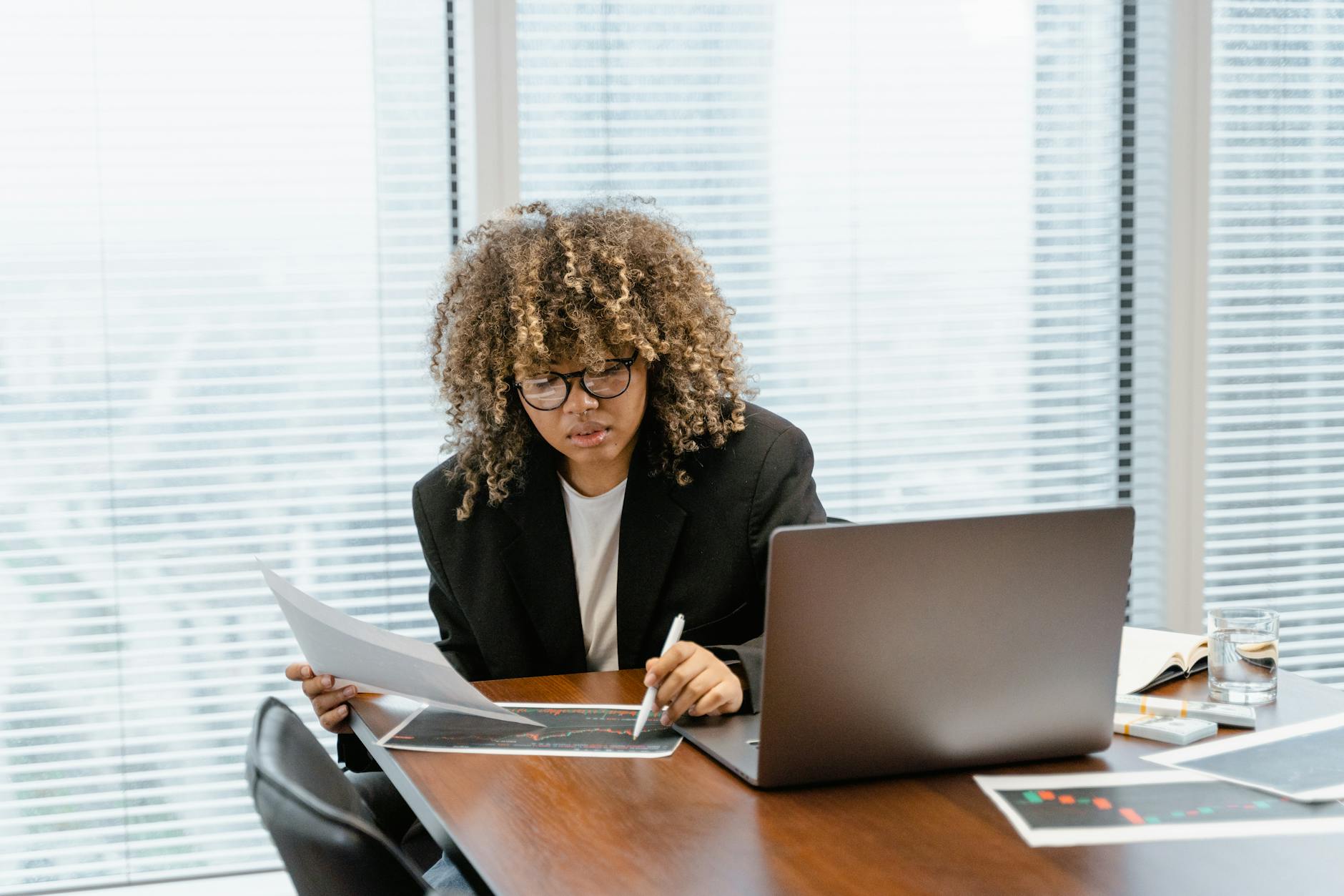 Young black woman sitting at conference table looking at papers next to her laptop.