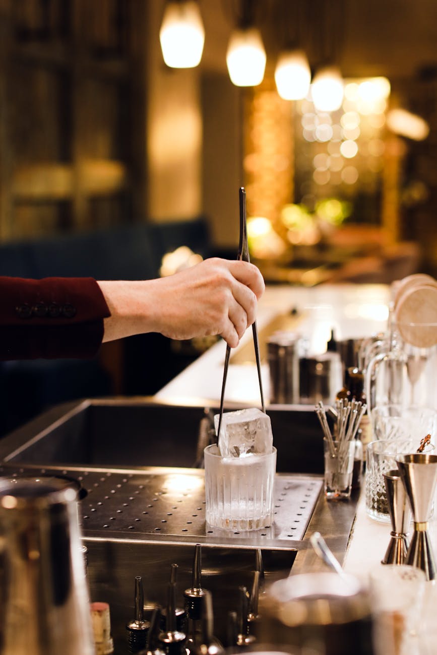 Bartender dropping a large block of ice into a cocktail glass with tongs.