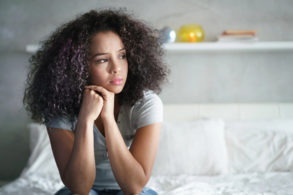Mixed woman lying on her bed looking to the left with her chin on her hands.