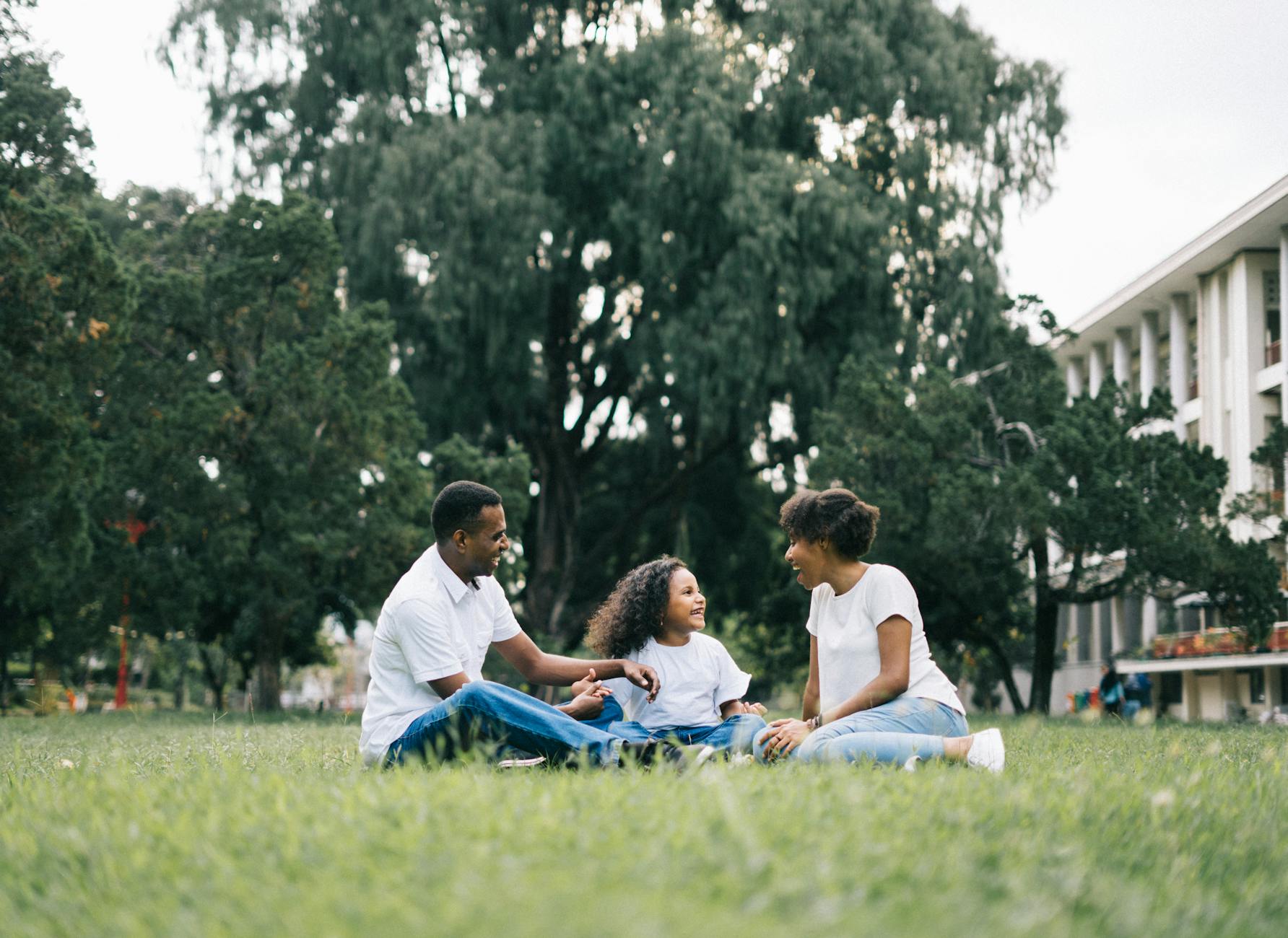 Black family sitting on the grass laughing.