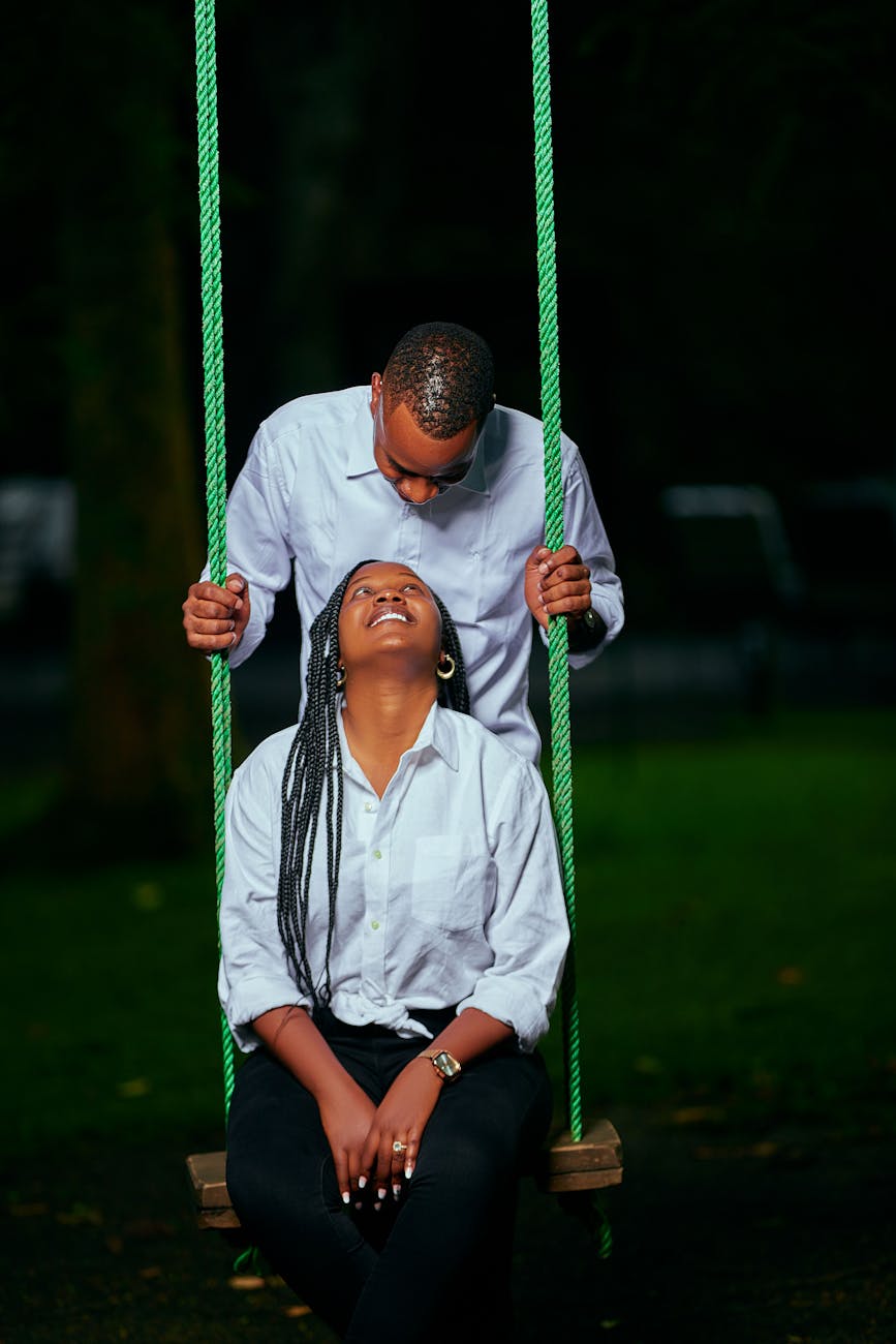 Black couple sitting on a swing smiling at each other.