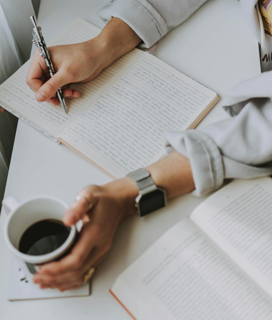 Woman sitting at desk with coffee and writing in planner.