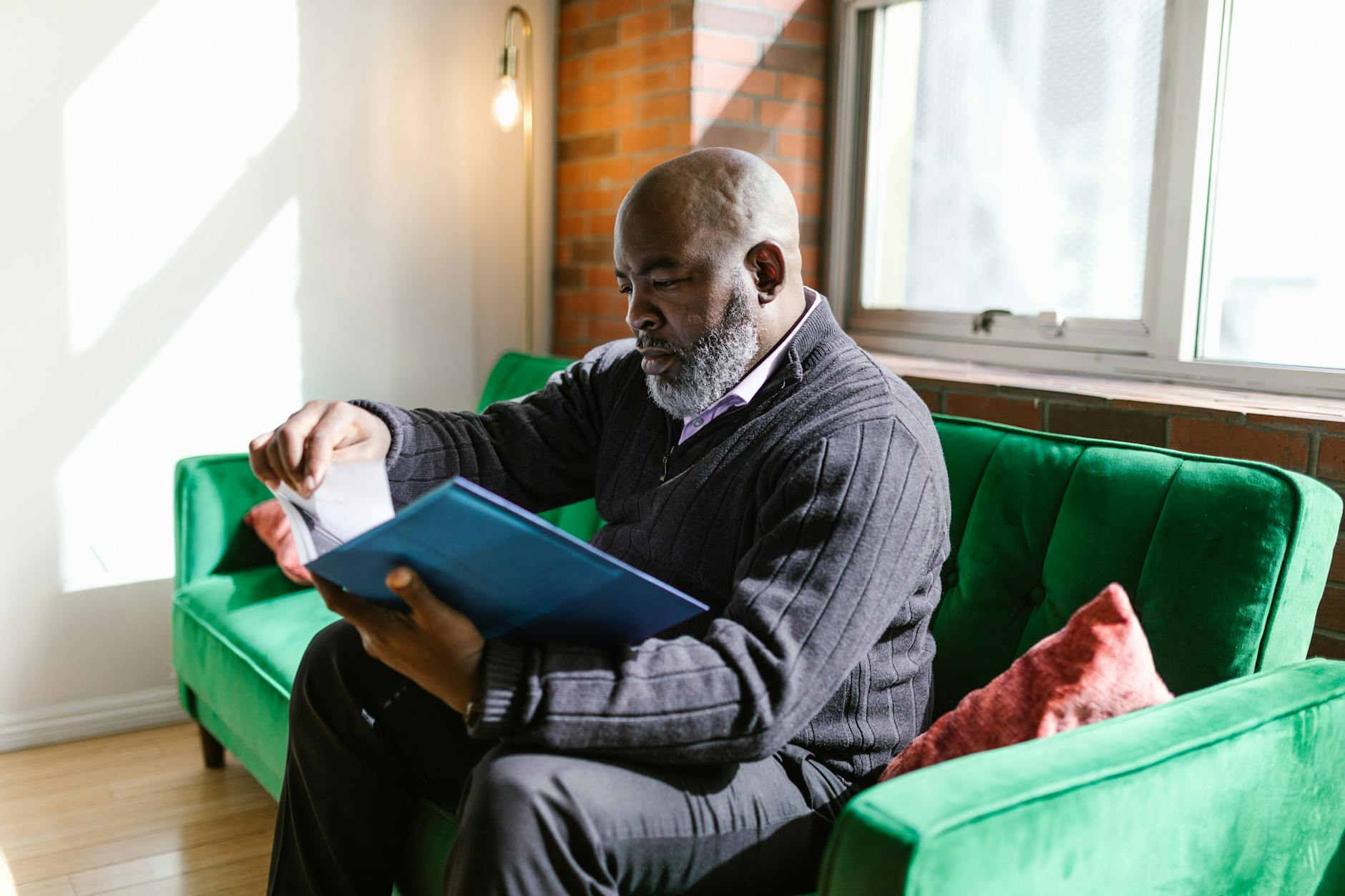 Mature Black man sitting on a green couch reading.