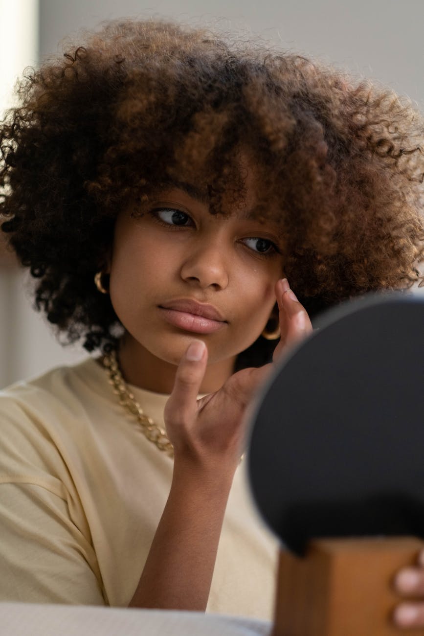 Young Black woman looking in a mirror examining herself.